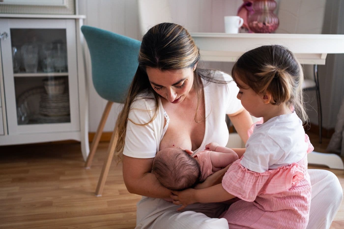 A mother breastfeeds her newborn while her toddler sits nearby