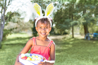 Easter basket ideas: Young girl wearing bunny ears and holding basket full of colored eggs