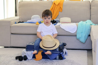 Toddler boy sitting on top of mother's suitcase looking a little sad.