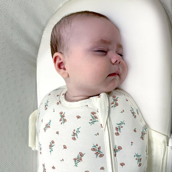 Baby sleeping swaddled on an Ivory Silk SNOO Sheet in the SNOO bassinet.