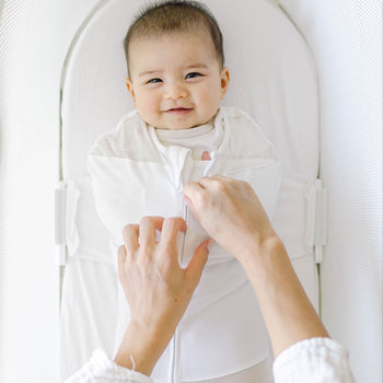Baby being zipped up in Ivory SNOO Sack in SNOO bassinet