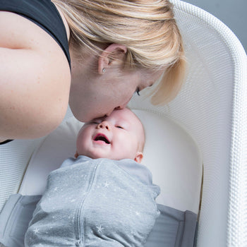 Mom kissing baby swaddled in Graphite Stars SNOO Sack in SNOO