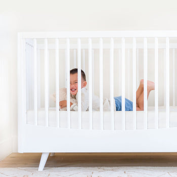Toddler laying in Lola Crib on Ivory Crib Sheet
