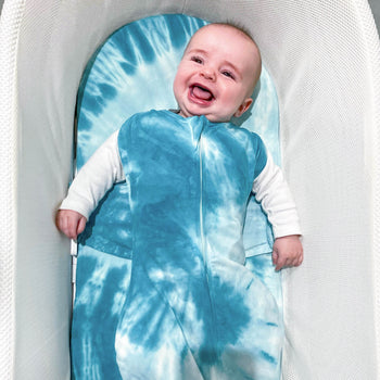 Baby smiling in SNOO with arms out in Blue Tie-Dye SNOO Sack on Blue Tie-Dye SNOO Sheet