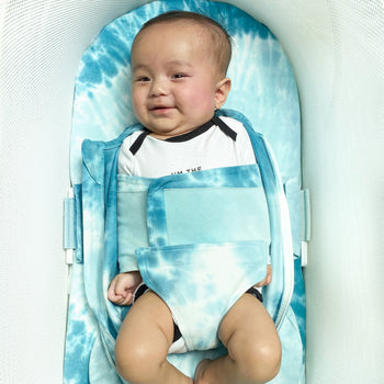 Baby smiling in Blue Tie-Dye SNOO Sack swaddled with arms down and sack unzipped on Blue Tie-Dye SNOO Sheet in SNOO