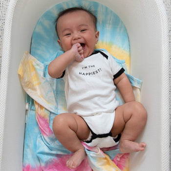 Baby wearing "I'm the Happiest" bodysuit in SNOO unswaddled with Rainbow Tie-Dye SNOO Sheet and Rainbow Tie-Dye SNOO Sack